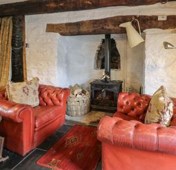 A living room with red leather armchairs a wood burning stove and a rug at Ty Fferm Hen in Talybont-on-Usk