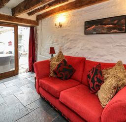 A living room with a red sofa and cushions a floor lamp and glass door leading outside at Ty Fferm Hen in Talybont-on-Usk