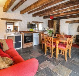 A rustic living area with wooden beams a red sofa a wooden dining table with chairs and a small kitchen at Ty  Fferm Hen in Talybont-on-Usk