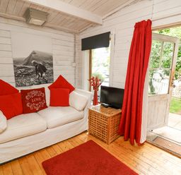 A living room with a white sofa with red pillows a small wooden table with a television and red curtains at Ty Bach Twt in Talybont-on-Usk