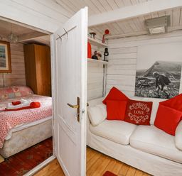 A small living area with a white sofa and red pillows next to a bedroom with a bed covered in patterned bedding at Ty Bach Twt in Talybont-on-Usk