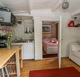 A small kitchen area with wooden counter and utensils next to a doorway leading to a bedroom with a bed covered in a patterned quilt at Ty Bach Twt in Talybont-on-Usk