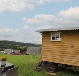 A wooden shepherds hut on wheels with a table and chairs on grass in a rural landscape at Ty Gwenyn in Talybont-On-Usk