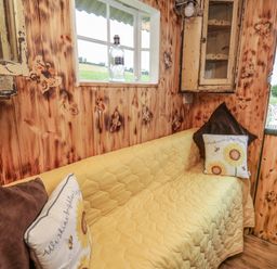 A small sitting area with a yellow quilted couch and floral pillows in a wooden room with butterfly designs at Ty Gwenyn in Talybont-On-Usk