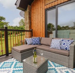 An outdoor seating area with a gray wicker sofa and blue patterned cushions on a deck with wooden railing at The Bothy Riding Hills Riding Mill near Corbridge
