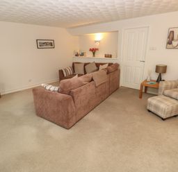 A living room with brown sofa and plaid armchair with ottoman at Flat 1 in Tenby