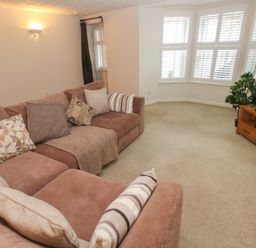 A living room with a brown sectional sofa with cushions a wooden TV stand with a TV and a plant near bay windows at Flat 1 in Tenby