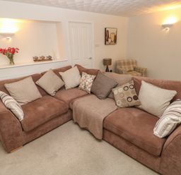 A living room with a brown sofa with cushions a beige armchair a lamp wall lights paintings and flowers on a shelf at Flat 1 in Tenby