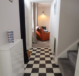 A hallway with black and white checkered floor leading to a room with an orange armchair and a gray carpet at White Feathers in Alnwick