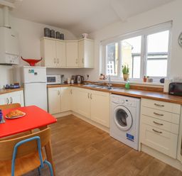 A kitchen with white cabinets a red table with chairs a washing machine and a window at White Feathers in Alnwick