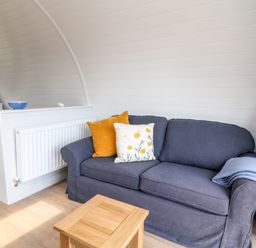 A living area with a blue sofa with cushions and a small wooden table near a bed at Oak in Elmgate near Saltash
