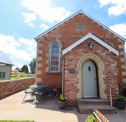 A brick building with an arched door and window a metal table with chairs and potted plants outside at The Old Chapel in Dorstone near Hay-on-Wye
