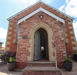 Brick building entrance with arched doorway and open door leading inside with outdoor seating and plants at The Old Chapel in Dorstone near Hay-on-Wye