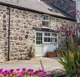 Stone exterior of a building with a pale green door and windows with potted plants and flowers outside at The Barn at Trevothen Farm Coverack