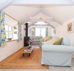 A long living room with sofas coffee table wood burner and curtains at The Barn at Trevothen Farm Coverack