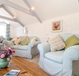 A living room with light blue armchairs and sofas with cushions and a wooden coffee table with flowers at The Barn at Trevothen Farm in Coverack