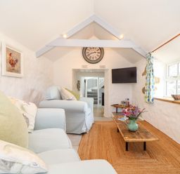 A sitting room with light blue sofas a wooden coffee table a wall clock mounted television and patterned curtains at The Barn at Trevothen Farm Coverack