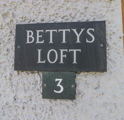 A black sign with white letters displaying Bettys Loft and the number 3 on a textured white wall