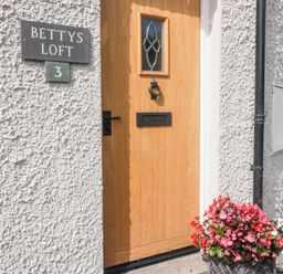 A wooden front door with a knocker and mail slot beside a sign that reads Bettys Loft 3 with a flower pot at Bettys Loft in Hawkshead