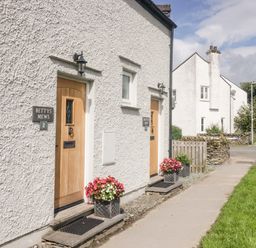 Exterior view of white buildings with wooden doors and flower pots on a sidewalk at Bettys Loft in Hawkshead