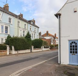 A street view with a white building with a blue door and pastel colored houses along a road at Braiders Rest in Bridport
