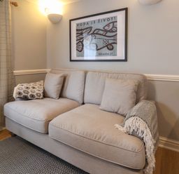 A beige sofa with cushions and throws under a framed fish artwork in a room at Braiders Rest in Bridport
