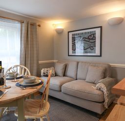 A dining area with a wooden table set with plates and glasses next to a beige sofa and framed artwork at Braiders Rest in Bridport