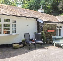 An outdoor seating area with two black chairs and a green bench in front of a white and stone building at Fell View Clappersgate near Ambleside