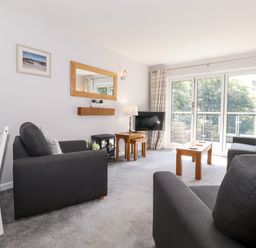A living room with grey sofas wooden tables a wall mirror and glass doors at Fell View in Clappersgate near Ambleside