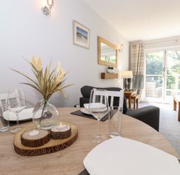 A dining table set with plates glasses and candles in a living room with sofas a lamp and large windows at Fell View in Clappersgate near Ambleside