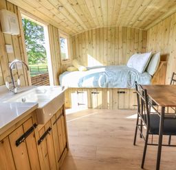 A small wooden room with a kitchen sink dining table chairs and a bed at The Oak Hut in Coton near Whitchurch
