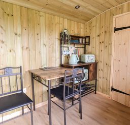 A wooden kitchen area with a table two chairs kettle toaster and shelves at The Oak Hut in Coton near Whitchurch