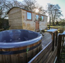 An outdoor wooden hut with two windows and a door next to a large round hot tub on a wooden deck at The Oak Hut in Coton near Whitchurch