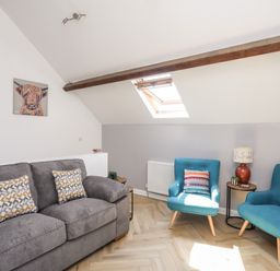 A living room with a grey sofa two blue armchairs a skylight window and a side table with a lamp at Stabal Bach in Criccieth