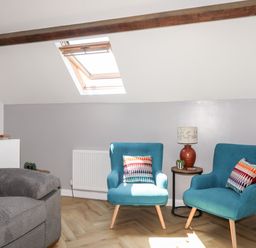 A sitting area with two blue chairs and a side table with a lamp and plants under a skylight at Stabal Bach in Criccieth