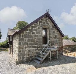 Stone building with metal stairs leading to a door and potted plant outside at Stabal Bach in Criccieth