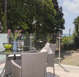 An outdoor patio with a glass table surrounded by wicker chairs and a vase with flowers at Stabal Bach in Criccieth