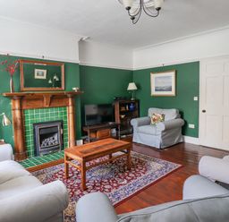 A living room with green walls a wooden fireplace a wooden coffee table two sofas and an armchair at Victoria House in Alnwick