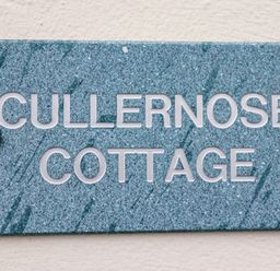 A blue speckled nameplate with white letters reading Cullernose Cottage mounted on a white wall at Cullernose Cottage in Newton-by-the-Sea near Embleton