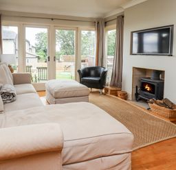 A living room with a beige sofa an ottoman a black armchair a fireplace and a wall-mounted TV at Cullernose Cottage Newton-by-the-Sea near Embleton