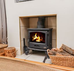 A wood burning stove with a fire burning inside a tiled fireplace with a basket of firewood nearby at Cullernose Cottage Newton-by-the-Sea near Embleton