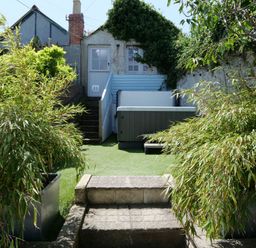A backyard with stone steps plants a hot tub and a small building at Waves End in St Ives