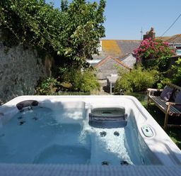 An outdoor hot tub with water surrounded by plants a wooden bench with cushions and a dining table at Waves End in St Ives