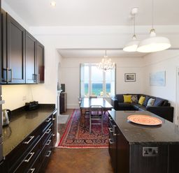A kitchen with black cabinets and a dining area with a wooden table and sofa at Waves End in St Ives