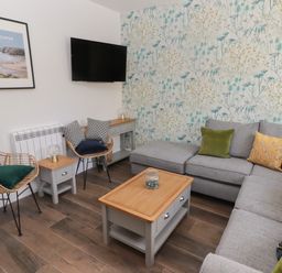 A living room with a grey corner sofa and wooden coffee table at Gwynfryn in Pen-Clawdd