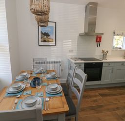 A kitchen with a wooden dining table set for six with blue placemats and grey chairs at Gwynfryn in Pen-Clawdd