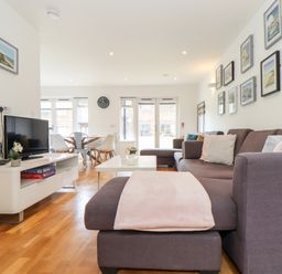 A living room with a brown sectional sofa and cushions a coffee table a tv on a white stand and a dining table with chairs at Garras in Porthtowan