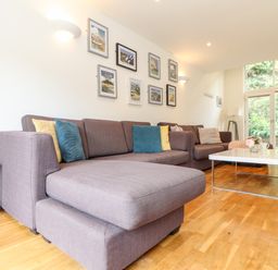 A living room with two brown sofas blue and yellow cushions white coffee table and framed pictures on wall at Garras in Porthtowan