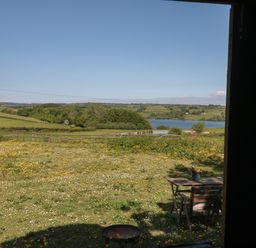 View of a field with wildflowers a wooden table with chairs and a lake in the distance at The Snug in Dulverton