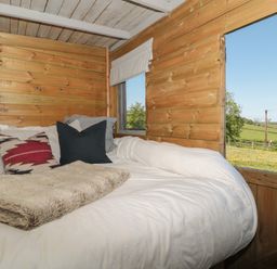 A bed with pillows and a blanket inside a wooden room with a window showing a green field at The Snug in Dulverton